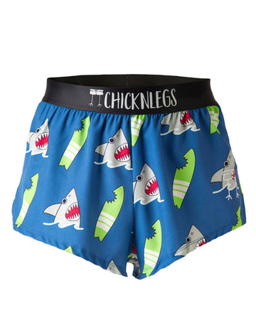 Chicknlegs men's 2 in split running shorts in the blue sharks design, as a ghost image. The print has a blue background with green surfboards with bite marks on it with a grey gray shark coming out of the water. These shorts are made for runners.