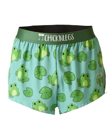 These chicknleg shorts are in the men's 2 in split running shorts as the fartlek frog design, as a ghost image. The print has frogs all over it with lilypads on a light blue background with a green waistband.