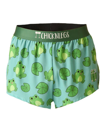 These chicknleg shorts are in the men's 2 in split running shorts as the fartlek frog design, as a ghost image. The print has frogs all over it with lilypads on a light blue background with a green waistband.