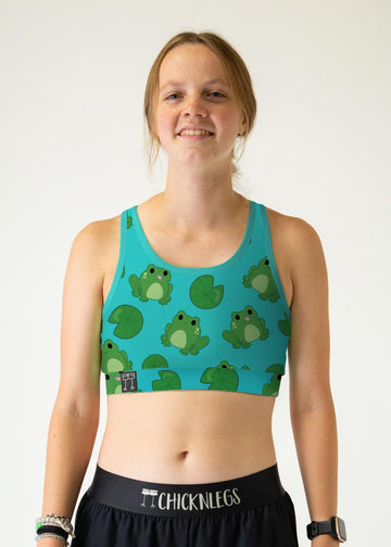 The model is a runner who is wearing Chicknlegs women's OG sports bra in the fartlek froggies design, facing front. A close up is shown.