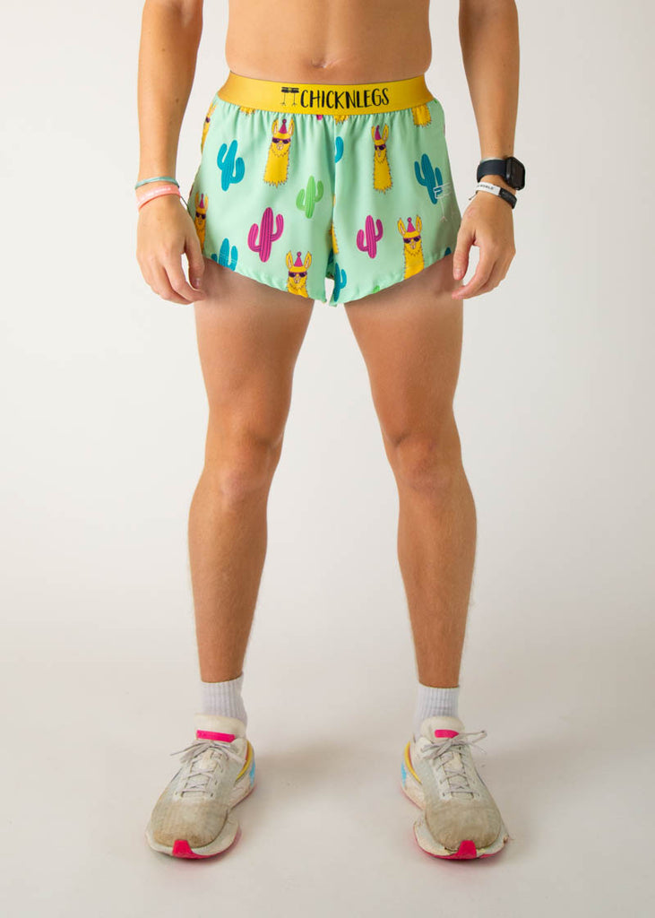 The model is a runner wearing Chicknlegs in men's 2 inch split running shorts in the green llama design, facing front.
