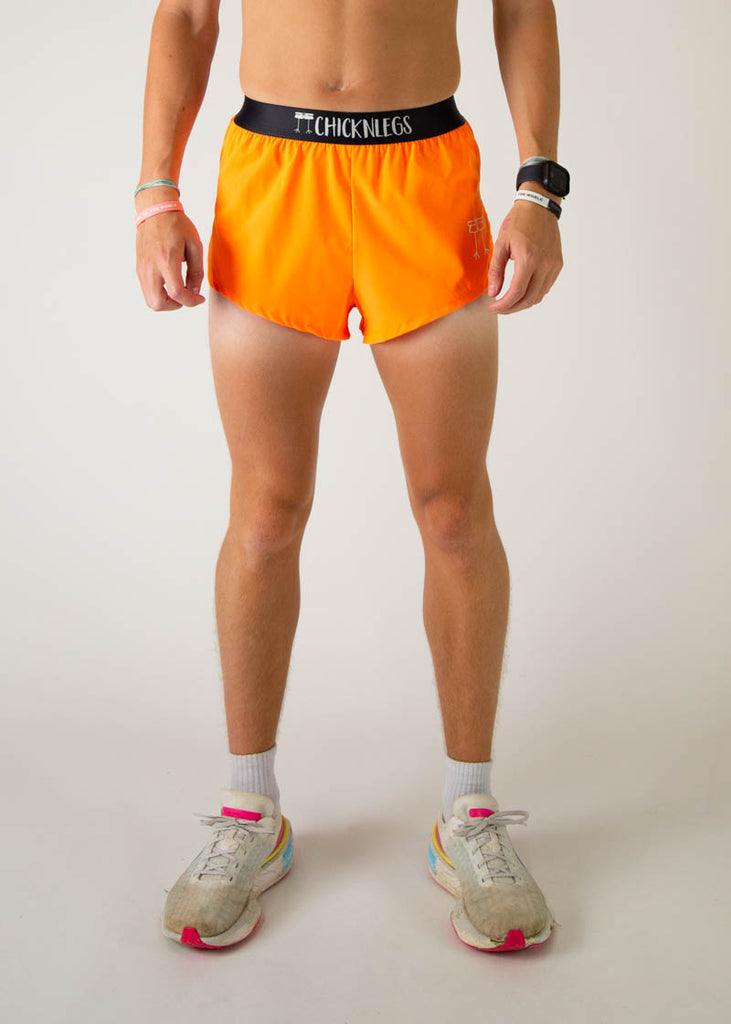 The model is a runner wearing Chicknlegs men's 2 inch split running shorts in the neon orange design, facing front.
