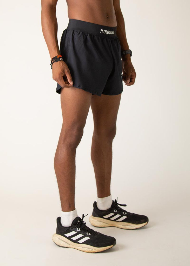 Model wearing Chicknlegs in mens 4 inch split running shorts in the black design, facing right.
