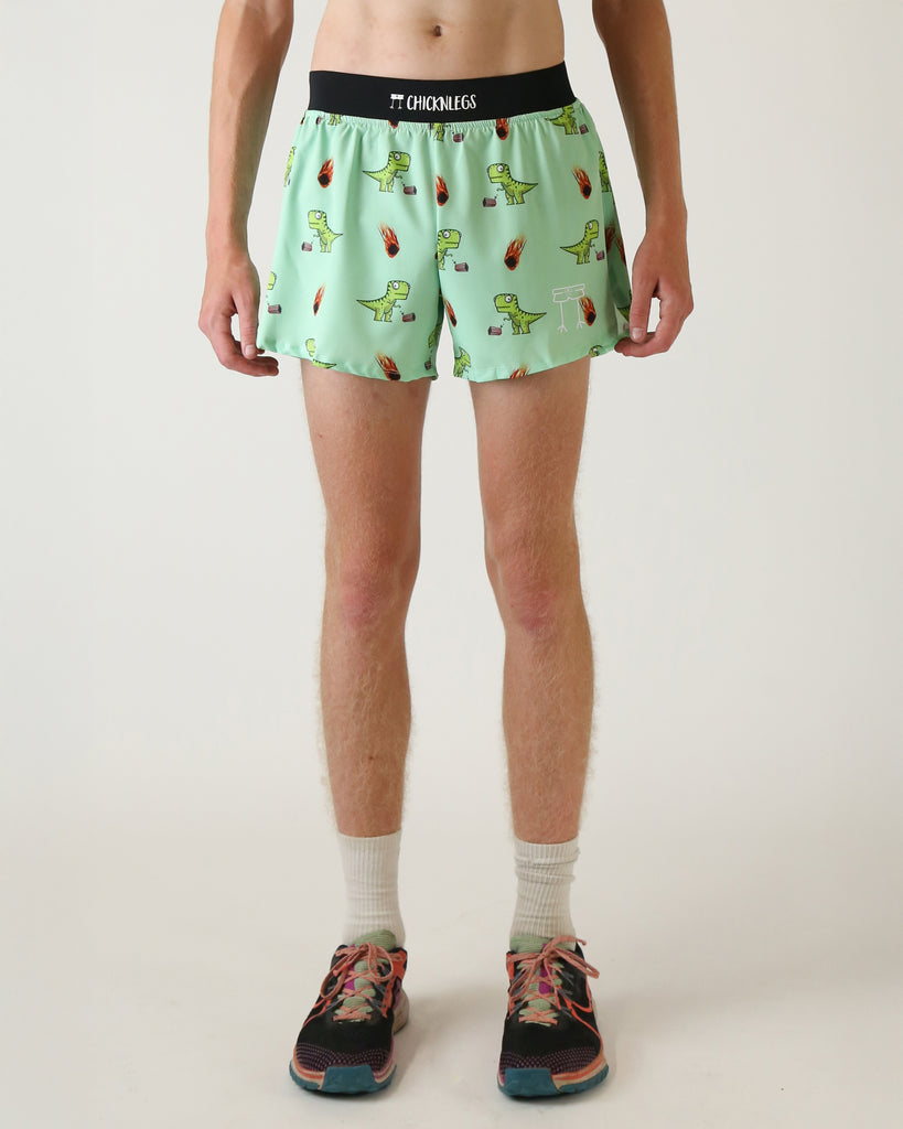 Runner is wearing ChicknLegs in the men's 4 in split running shorts with a back pocket and inner liner pocket. The print has dinosaurs on it with popcorn and a meteor. The dinosaur is green on a light green background.