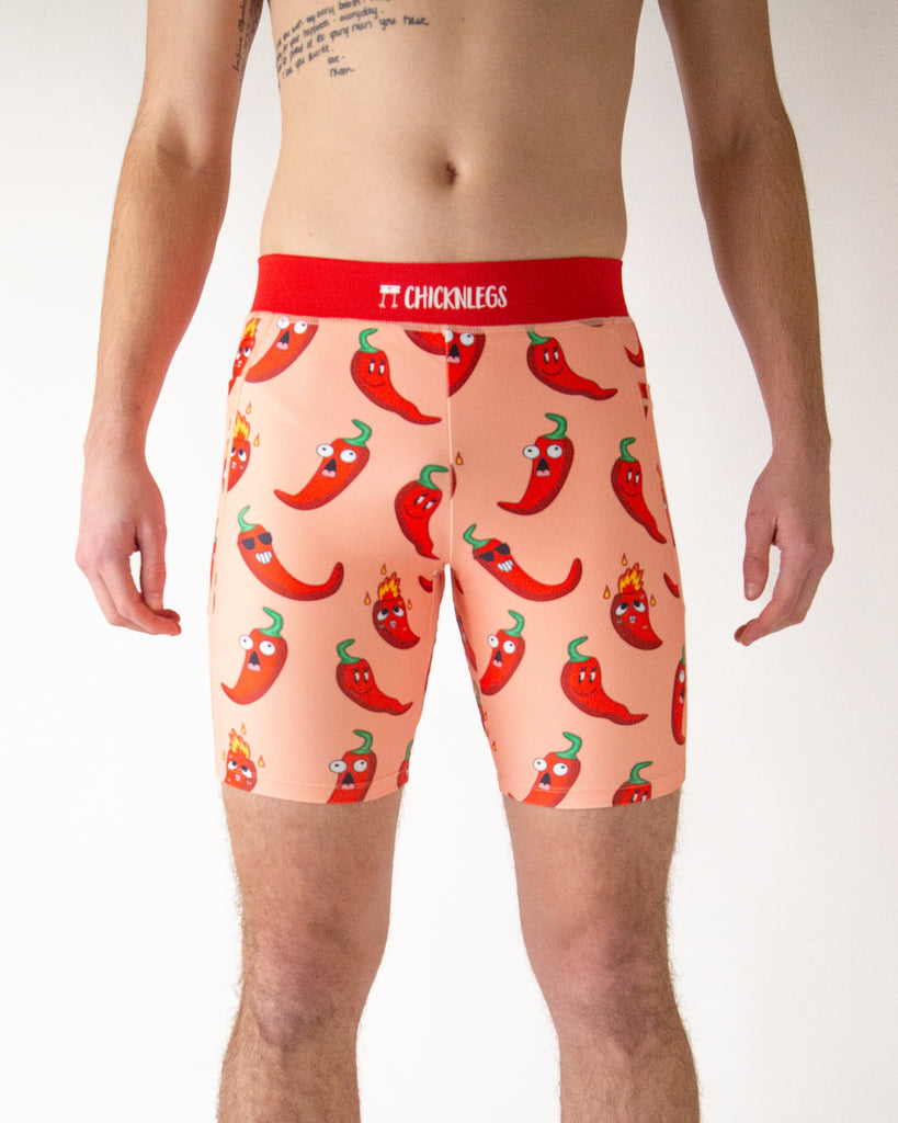 Runner is wearing ChicknLegs in the men's 8 in half tights with pockets in the chili peppers design. The print has fun red chili peppers with sunglasses and fire on a light solid orange color background.