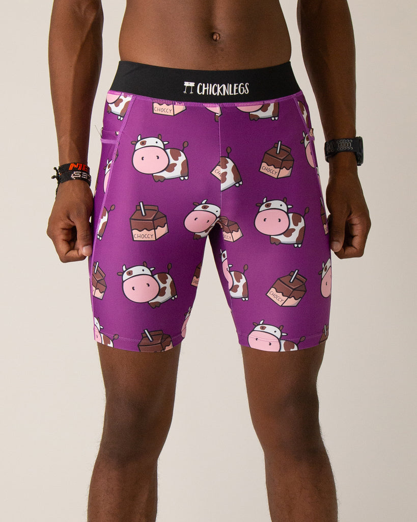 Runner is wearing ChicknLegs in the men's 8 in half tights with pockets in the choccy cow design. The print has fun brown and white cows on it with chocolate milk cartons on a solid purple background.