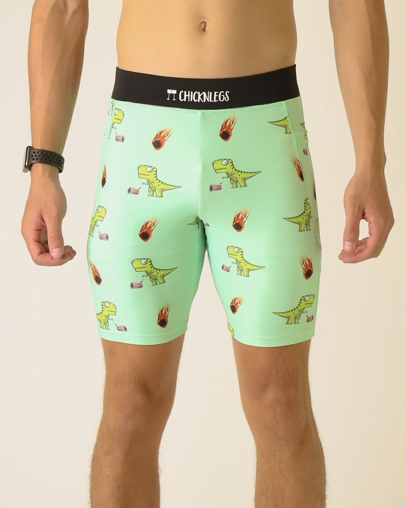 Runner is wearing ChicknLegs in the men's 8 in half tights with pockets in the dino-sore design. The print has green dinosaurs on it with popcorn and a meteor, on a light green solid color background.