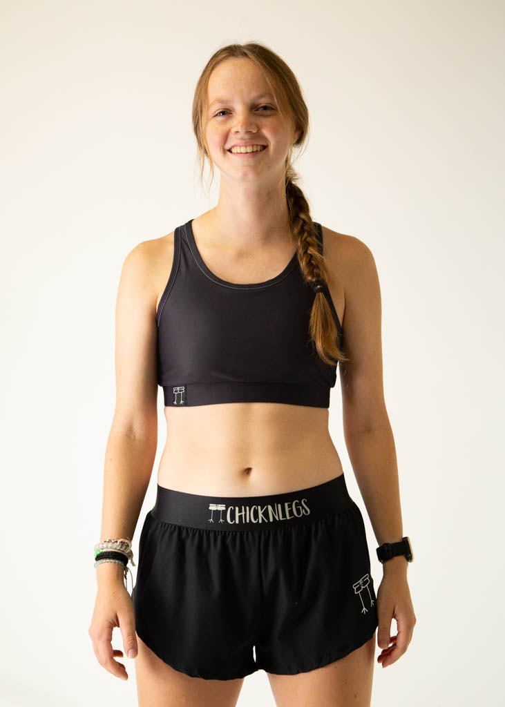 The model is a runner wearing Chicknlegs women's OG sports bra in the black design, facing front. 