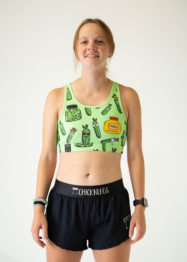 The model is a runner who is wearing Chicknlegs women's OG sports bra in the pickles design, facing front.