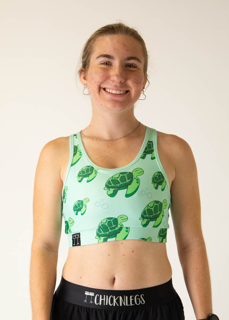 The model is a runner who is wearing Chicknlegs OG sports bra in the turtles design, facing front. A close up is shown.