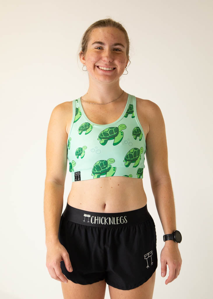 The model is a runner who is wearing Chicknlegs OG sports bra in the turtles design, facing front.