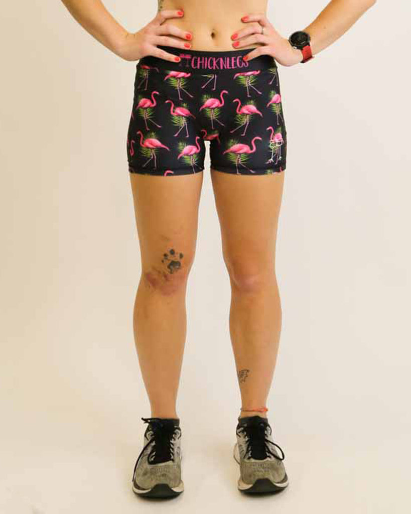 Runner is wearing ChicknLegs in the women's 3 in compression spandex shorts with the black flamingo design. The print has pink flamingos on it with green leaves on a black background.