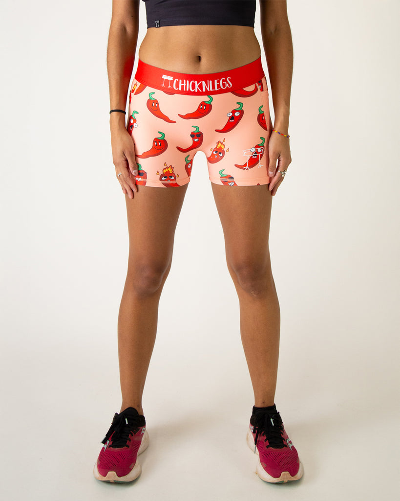 Runner is wearing ChicknLegs in the women's 3 in compression spandex shorts. The print has chili peppers on it with fun sunglasses and fun faces and sizes. They are red on a light orange red background.