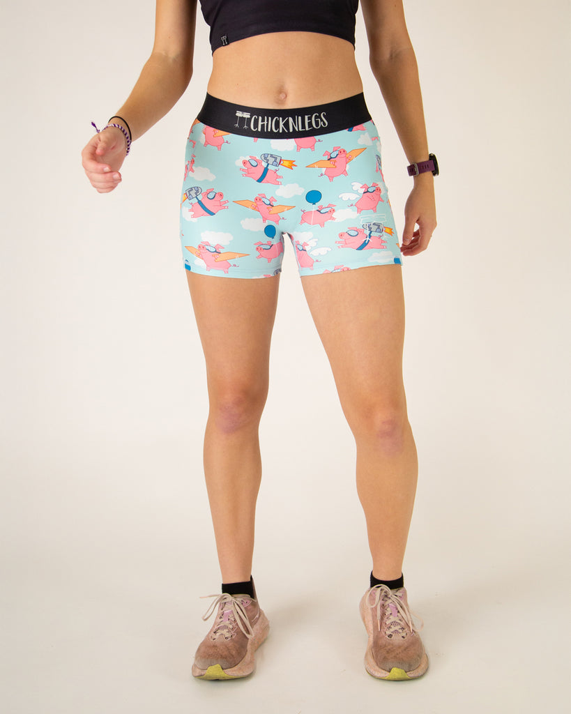 Runner is wearing ChicknLegs in the women's 3 in compression spandex shorts with side panel pockets that fit high rise on the waist. The print has flying pigs on it with clouds.