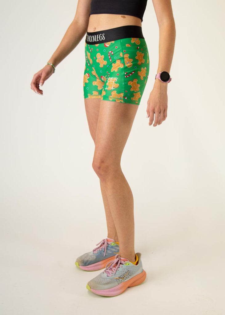 The model is a runner who is wearing Chicknlegs women's 3" compression shorts in the Gingerbread Men Gingy's Revenge design, facing left.