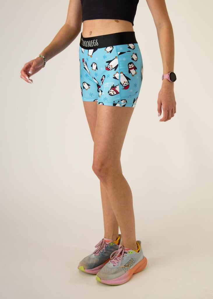 The model is a runner who is wearing Chicknlegs in Women's 3" compression shorts in the Slippery Bois, Penguins design, facing left.