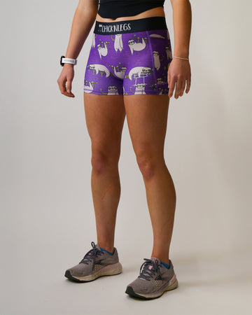 Runner is wearing ChicknLegs in the women's 3 in compression spandex in the sloth design. The print has sloths over it with leaves and branches on a purple background.