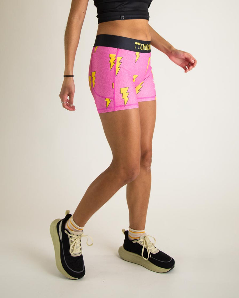 Runner is wearing ChicknLegs in the women's 3 in compression spandex with pockets shorts in the hot pink bolts design. The print has yellow lightning bolts on it with a hot neon pink background. 