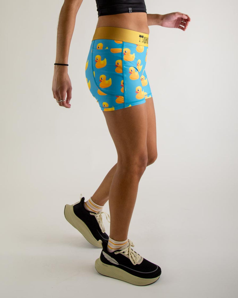 Runner is wearing ChicknLegs in the women's 3 in compression spandex shorts with pockets in the rubber ducky design. The print has yellow rubber ducks on it with a blue background. The model is facing right.