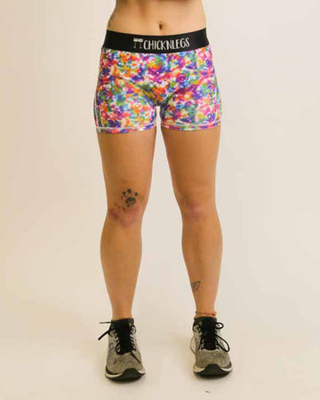 Runner is wearing ChicknLegs in the women's 3 in compression spandex shorts in the tie-dye design. The print is a mix of fun colors of the rainbow of green, yellow, orange, pink, red, purple, and blue.