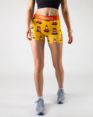 Runner is wearing ChicknLegs in the women's 3 in compression spandex shorts in the traffic cones design. The print has orange traffic cones on a fun yellow orange background.