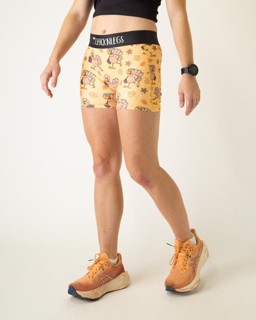 The model is a runner who is wearing Chicknlegs women's 3 inch compression shorts in the pardoned turkey design, facing left.