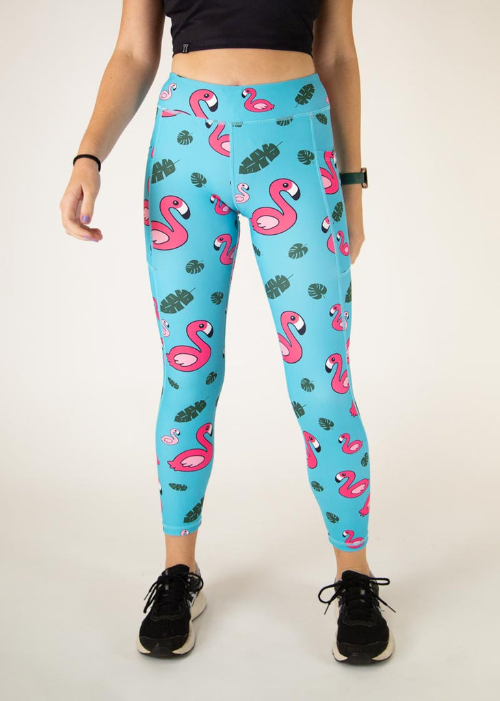 The model is a runner who is wearing Chicknlegs Women's Leggings in the Blue Flamingo design. These leggings include side pockets and an adjustable drawstring at the front. The model is facing front.