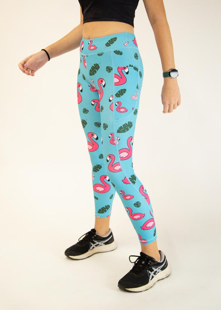 The model is a runner who is wearing Chicknlegs Women's Leggings in the Blue Flamingo design. These leggings include side pockets and an adjustable drawstring at the front. The model is facing slightly left.