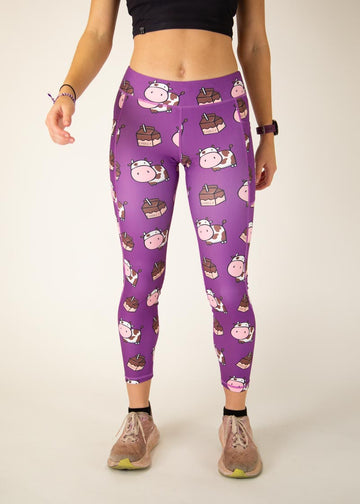 The model is a runner who is wearing Chicknlegs Women's Leggings in the Choccy Cow design. These leggings include side pockets and an adjustable drawstring at the front. The model is facing front.