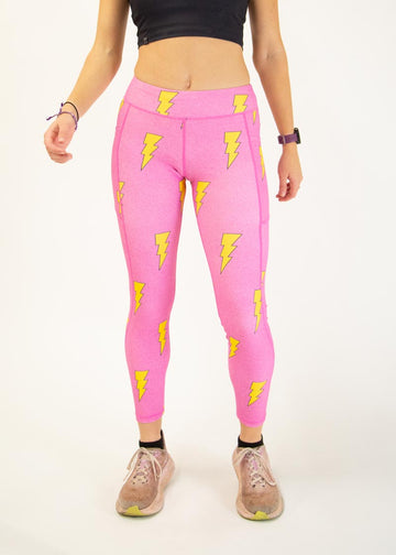 The model is a runner who is wearing Chicknlegs Women's Leggings in the Hot Pink Bolts design. These leggings include side pockets and an adjustable drawstring at the front. The model is facing front.