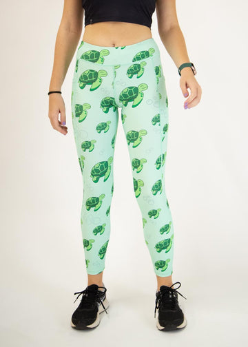 The model is a runner who is wearing Chicknlegs Women's Leggings in the Sea Turtles design. These leggings include side pockets and an adjustable drawstring at the front. The model is facing front.