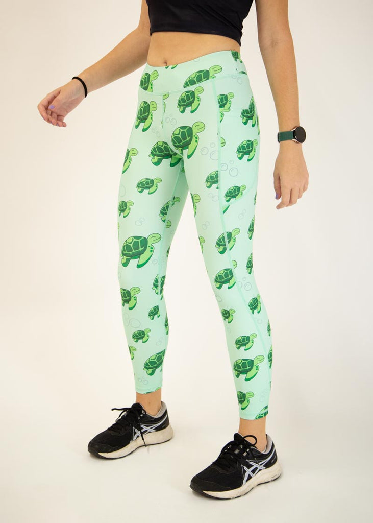 The model is a runner who is wearing Chicknlegs Women's Leggings in the Sea Turtles design. These leggings include side pockets and an adjustable drawstring at the front. The model is facing slightly left to show the side.