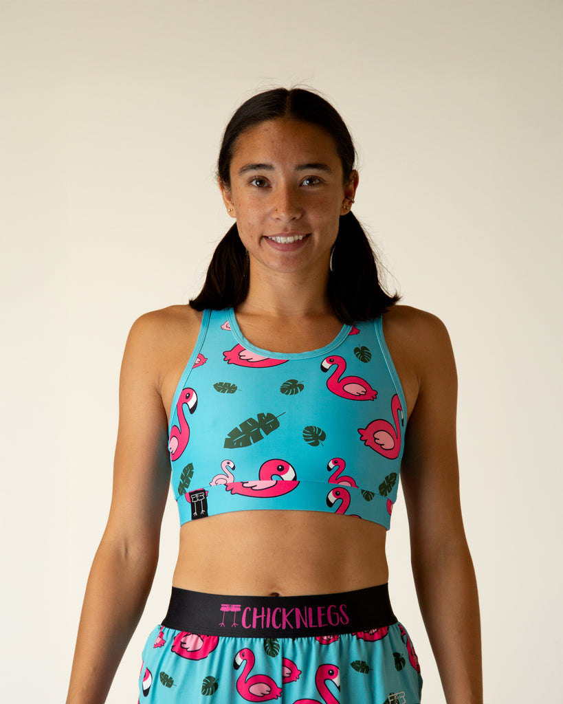 Runner is wearing ChicknLegs in the women's OG Sports Bra has a back pocket for exercise, running, workout, gym, and every day lifestyle. The print is the blue flamingo which has pink flamingos, green leaves and a blue background.