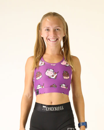 Runner is wearing ChicknLegs in the women's OG Sports Bra has a back pocket for exercise, running, workout, gym, and every day lifestyle. The print is the choccy cow design with brown and white cows, chocolate milk and a purple solid background.