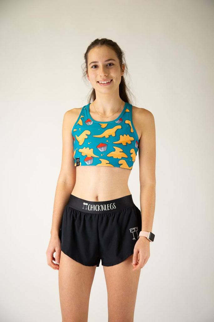 The model is a runner who is wearing Chicknlegs in the OG sports bra, in the dino nuggets design, facing front. 