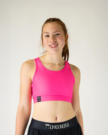 Runner is wearing ChicknLegs in the women's OG Sports Bra has a back pocket for exercise, running, workout, gym, and every day lifestyle. The print is the solid neon pink design, great for matching with the blue flamingos or for holidays such as valentines day.