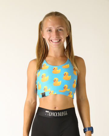 Runner is wearing ChicknLegs in the women's OG Sports Bra has a back pocket for exercise, running, workout, gym, and every day lifestyle. The print is the rubber duckys which has yellow ducks on a light blue solid background.