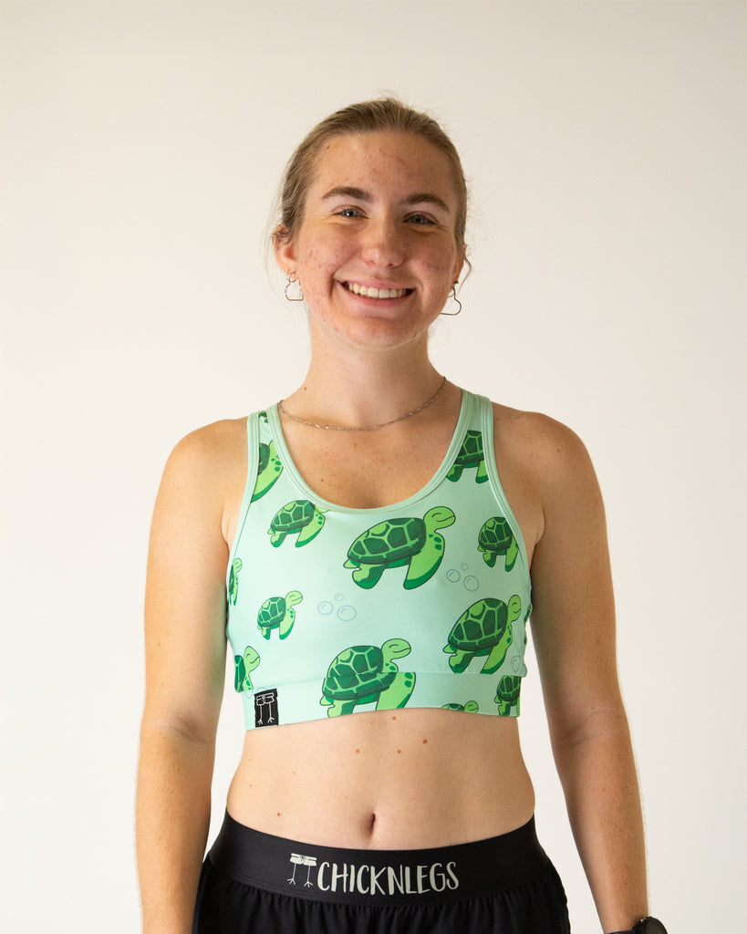 Runner is wearing ChicknLegs in the women's OG Sports Bra has a back pocket for exercise, running, workout, gym, and every day lifestyle. The print is the sea turtles design which has bubbles, green turtles on a light green background.