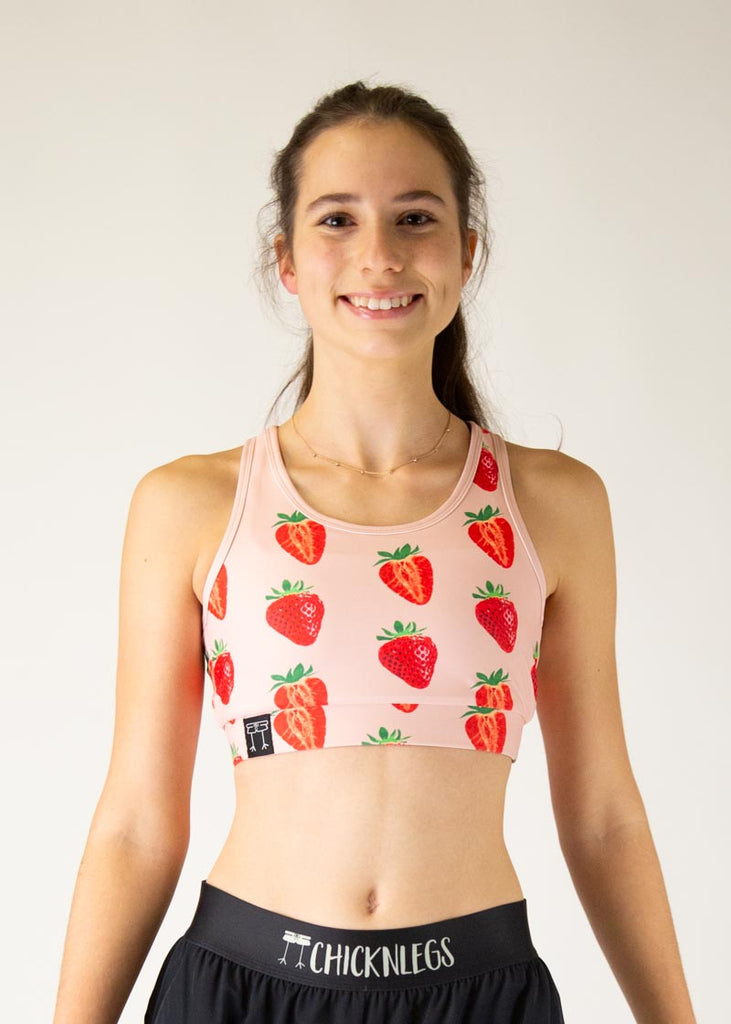 The model is a runner who is wearing Chicknlegs in the women's OG sports bra, in the strawberry SZN design, facing front. A close up of the model is shown in the photo.