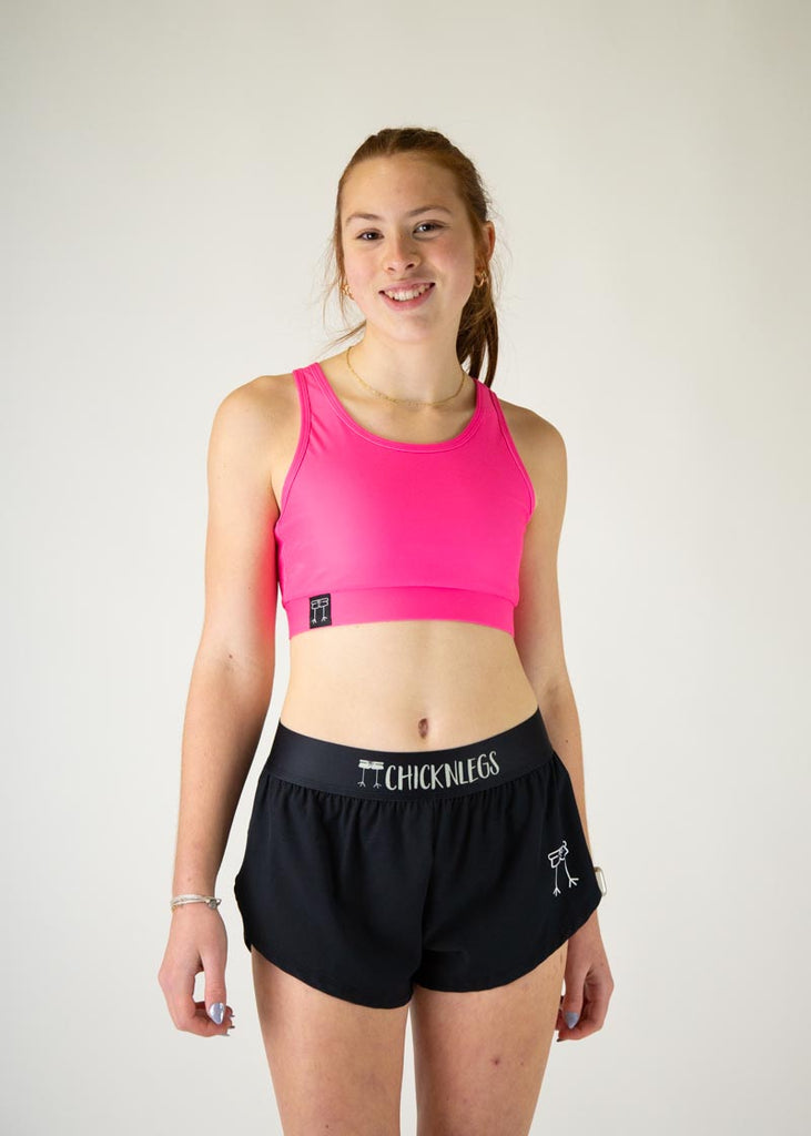 The model is a runner who is wearing Chicknlegs in the women's OG sports bra in the neon pink design, facing front.