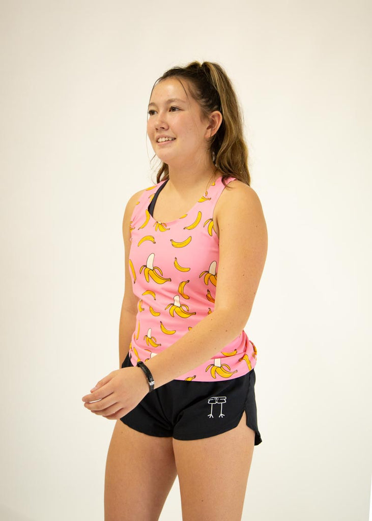 The model is a runner who is wearing Chicknlegs women's performance singlet in the pink banana design, facing  left.