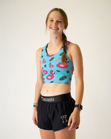 Runner is wearing ChicknLegs in the women's power crop top in the blue flamingo design. The material is lightweight and the print has pink flamingos on it with green leaves and a solid blue background.