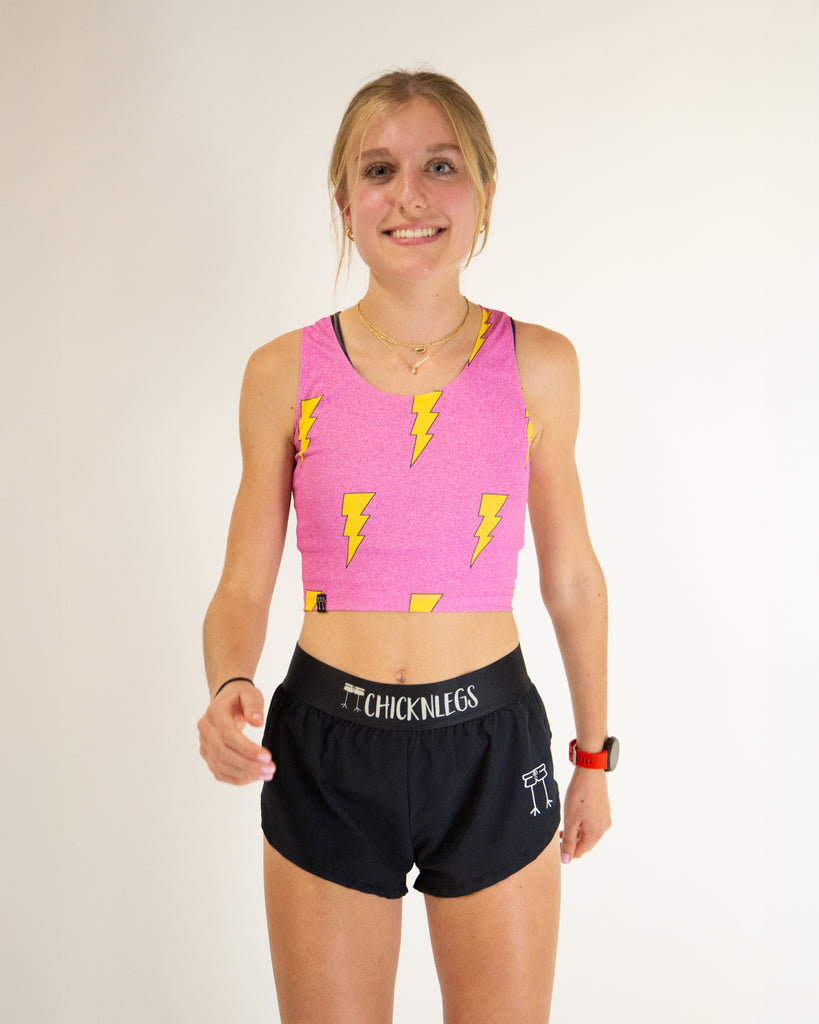 Runner is wearing ChicknLegs in the women's power crop top in the hot pink bolts design. The material is lightweight and the print has yellow lightning bolts and a hot pink background.