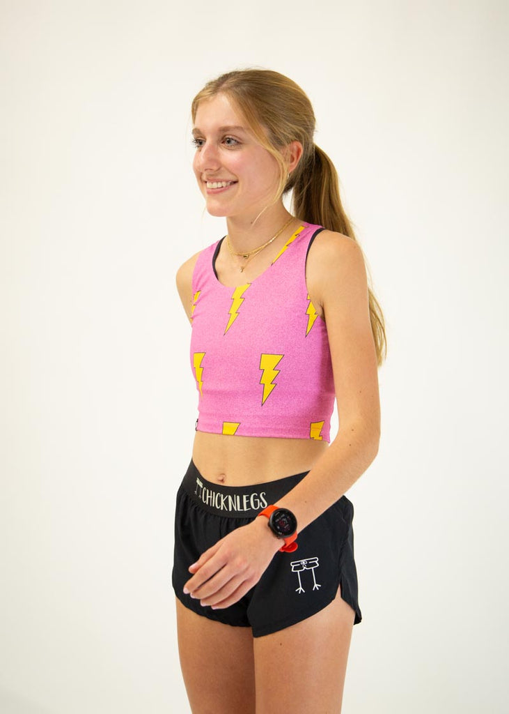 The model is a runner wearing Chicknlegs pwr crop top in the hot pink bolts design, facing left.