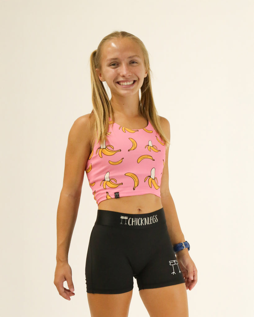 Runner is wearing ChicknLegs in the women's power crop top in the pink bananas design. The material is lightweight and the print has yellow bananas and a pink background.