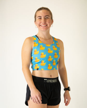 Runner is wearing ChicknLegs in the women's power crop top in the rubber duckys design. The material is lightweight and the print has yellow rubber ducks on it with a blue background.