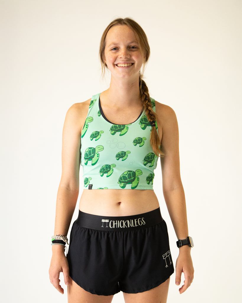 Runner is wearing ChicknLegs in the women's power crop top in the sea turtles design. The material is lightweight and the print has bubbles and green turtles on it with a light green solid background.