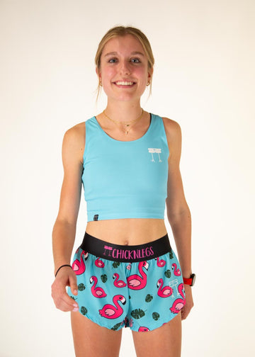 The model is a runner who is wearing Chicknlegs women's pwr crop top in the sky blue design, facing front. The model is matching the pwr crop with the women's 1.5" split running shorts in the blue flamingo design. The model is facing front.