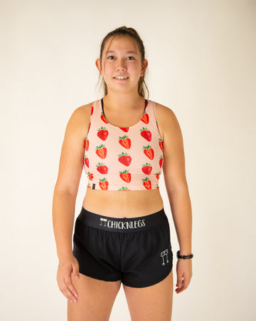 Runner is wearing ChicknLegs in the women's power crop top in the strawberry szn design. The material is lightweight and the print has red and pink strawberries over it.