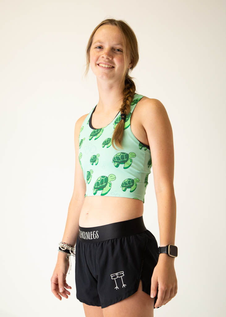 The model is a runner who is wearing Chicknlegs PWR crop top in the turtles design, facing left.